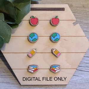 Peut inclure: Un ensemble de six boucles d'oreilles en bois avec différents motifs sur le thème de l'école. Les boucles d'oreilles présentent une pomme rouge, un globe terrestre bleu et vert, un crayon jaune et une pile de livres colorés.