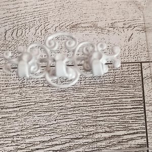 Op de afbeelding: Witte metalen wandhaak met een sierlijk, krullend ontwerp. De haak heeft drie afzonderlijke haken, elk met een gebogen vorm. Het decoratieve stuk is gemaakt van metaal en is wit geschilderd. De haak is ontworpen om items op te hangen.