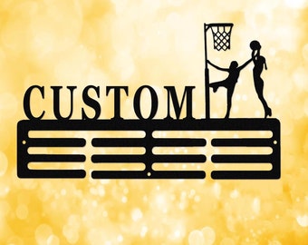 Puede incluir: Expositor de medallas de metal negro con la palabra "CUSTOM" y una silueta de dos mujeres jugando al netball. El expositor tiene seis filas de ganchos para colgar medallas.