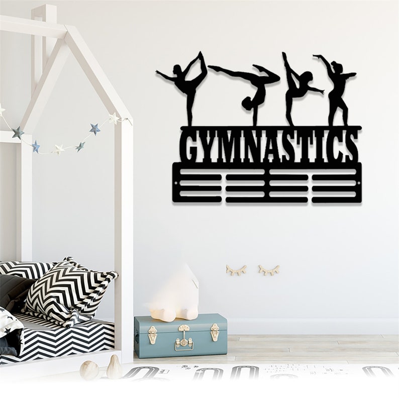 May include: Black metal gymnastics medal display with silhouettes of gymnasts in various poses. The display has the word "GYMNASTICS" in bold letters and eight slots for medals.
