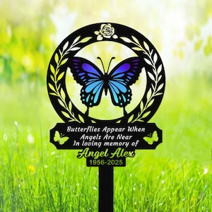 May include: Black metal garden stake with a butterfly silhouette and a memorial plaque. The plaque reads "Butterflies Appear When Angels Are Near In loving memory of Angel Alex 1956-2025".