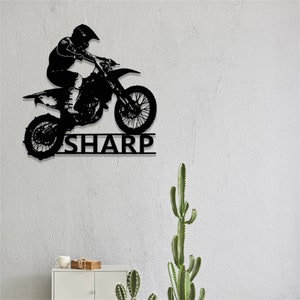 Op de afbeelding: Zwarte metalen silhouet van een motorcrossrijder die springt op een crossmotor met de naam "SHARP" eronder.