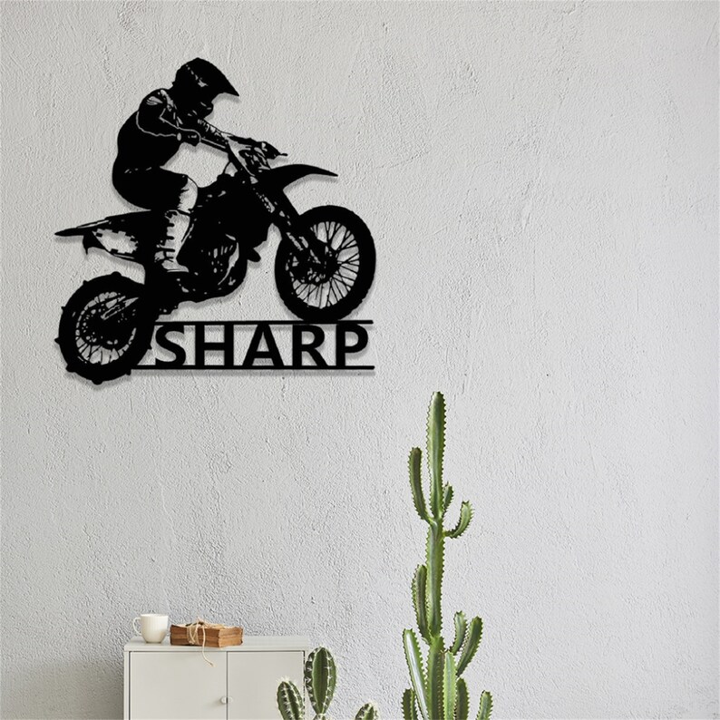 Op de afbeelding: Zwarte metalen silhouet van een motorcrossrijder die springt op een crossmotor met de naam "SHARP" eronder.