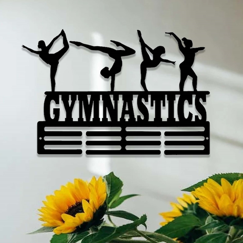 May include: Black metal gymnastics medal display with the word "GYMNASTICS" in bold letters. The display has 10 slots for medals and features silhouettes of gymnasts in various poses.