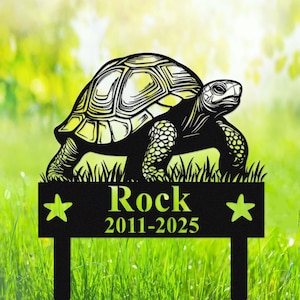 Könnte beinhalten: Schwarzer Metall-Gartenstecker mit einer Schildkröten-Silhouette. Der Stecker trägt den Namen "Rock" und die Jahreszahlen "2011-2025", mit Stern-Akzenten. Verschwommener grüner Hintergrund.