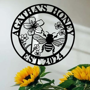 Op de afbeelding: Zwart metalen bord met de tekst "Agatha's Honey Est 2024" in een cirkel. Het bord toont een bij en bloemen.