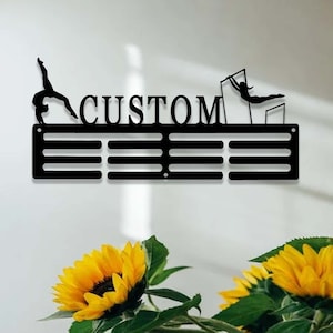 May include: Black metal medal display rack with the word "CUSTOM" in large letters. The rack has 8 slots for medals and features a gymnast silhouette on each end.