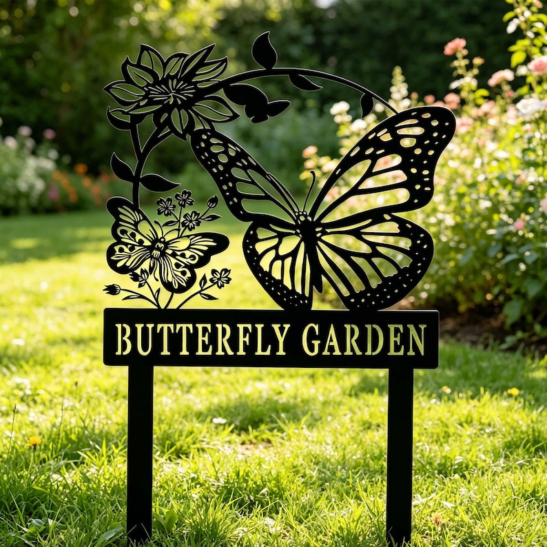 Puede incluir: Letrero de jard&iacute;n de metal negro con dise&ntilde;o de mariposa y flores. El letrero dice "BUTTERFLY GARDEN" en letras doradas. El letrero est&aacute; colocado en una zona de c&eacute;sped con flores en el fondo.