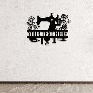 May include: Black metal wall art featuring a sewing machine design with floral accents. The text "YOUR TEXT HERE" is displayed prominently. Includes depictions of sewing tools like a needle, thread, and scissors. Ideal for a craft room or sewing enthusiast.