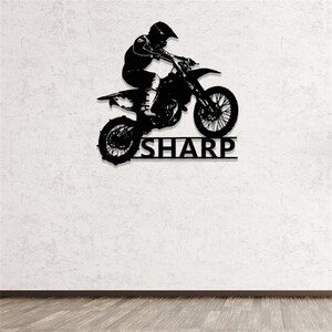 Op de afbeelding: Zwarte metalen silhouet van een motorcrossrijder die springt op een crossmotor met de naam "SHARP" eronder.