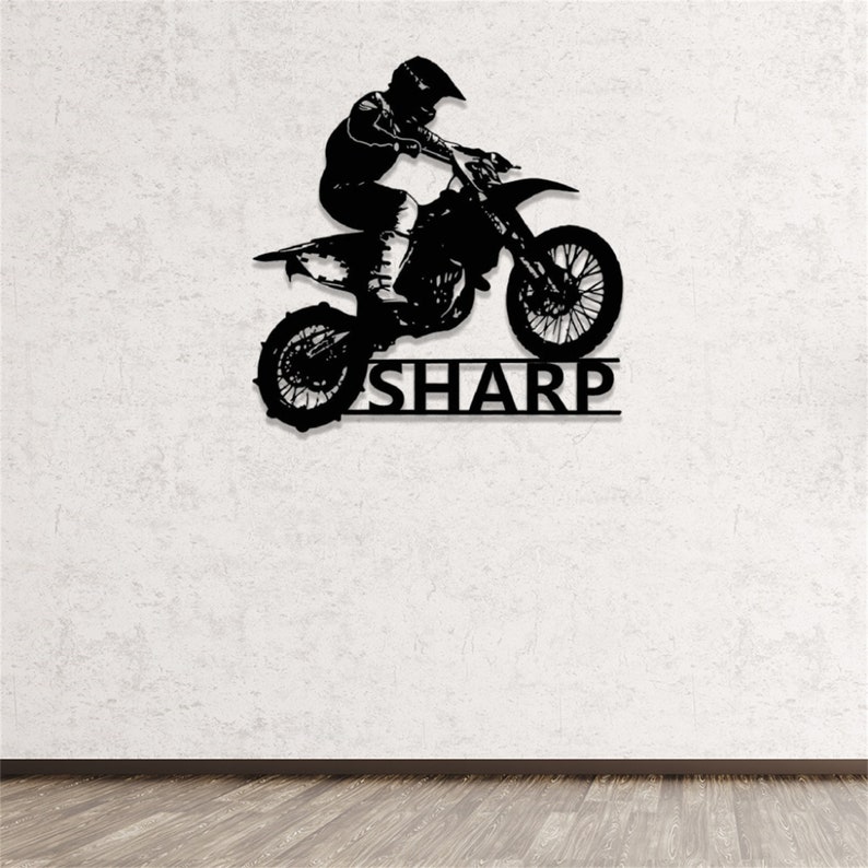 Op de afbeelding: Zwarte metalen silhouet van een motorcrossrijder die springt op een crossmotor met de naam "SHARP" eronder.