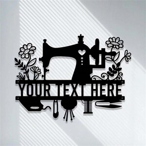 May include: Black metal wall art featuring a sewing machine silhouette with floral accents. The design includes the text "YOUR TEXT HERE" and sewing-related tools like scissors and a pin. A heart shape is incorporated into the sewing machine design.