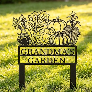 May include: A black metal garden stake featuring a cutout design of various vegetables including pumpkins, corn, and leafy greens. Below the produce, the text GRANDMA'S GARDEN is cut out in capital letters. The sign has two vertical stakes.