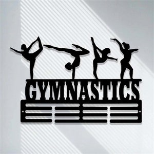 May include: Black metal gymnastics medal display with five gymnast silhouettes and the word "GYMNASTICS" in bold letters. The display has 12 slots for medals.