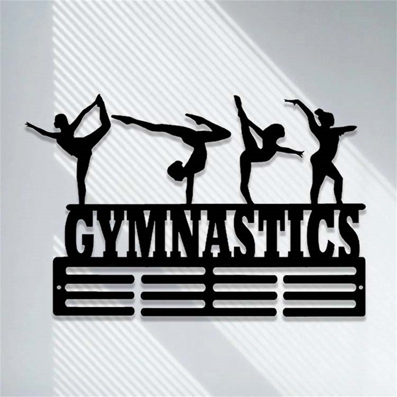 May include: Black metal gymnastics medal display with five gymnast silhouettes and the word "GYMNASTICS" in bold letters. The display has 12 slots for medals.