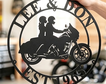 May include: A circular black metal wall sign featuring a silhouette of two people riding a motorcycle. The text LEE & DON is arched across the top, and EST. 1965 is arched along the bottom. The design is cut from a single piece of dark metal.