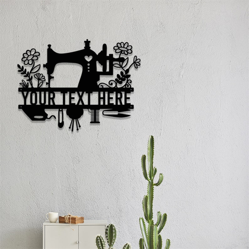 May include: Black metal wall art featuring a sewing machine design with floral accents. The text "YOUR TEXT HERE" is displayed below the sewing machine. Includes images of sewing tools. Decorative item for a craft room.
