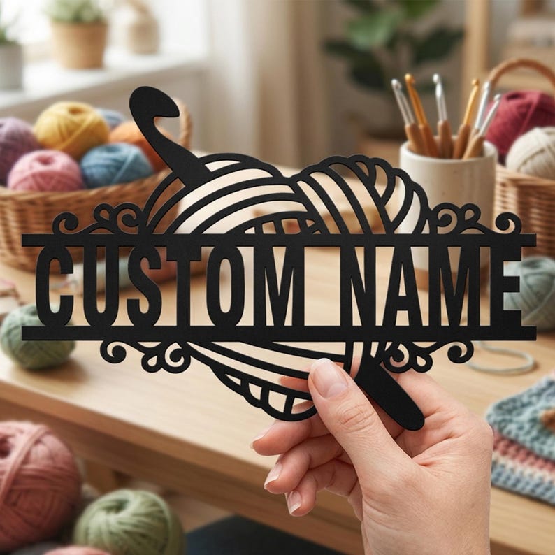 Pode incluir: Uma placa preta cortada a laser com um novelo de l&atilde; estilizado e uma agulha de croch&ecirc;, com o texto CUSTOM NAME centralizado em uma barra horizontal. O design inclui detalhes decorativos em espiral nos lados esquerdo e direito do texto.