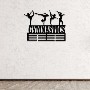 May include: Black metal gymnastics medal display with five gymnast silhouettes and the word "GYMNASTICS" above a row of medal hooks.