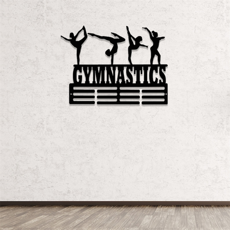 May include: Black metal gymnastics medal display with five gymnast silhouettes and the word "GYMNASTICS" above a row of medal hooks.