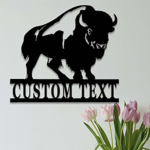 K&ouml;nnte beinhalten: Schwarze Metallsilhouette eines Bisons mit dem Text "CUSTOM TEXT" darunter. Die Silhouette ist an einer wei&szlig;en Wand montiert.