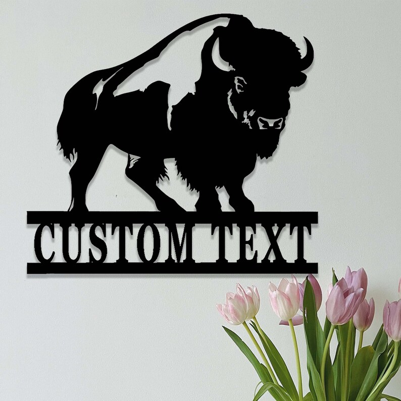 K&ouml;nnte beinhalten: Schwarze Metallsilhouette eines Bisons mit dem Text "CUSTOM TEXT" darunter. Die Silhouette ist an einer wei&szlig;en Wand montiert.