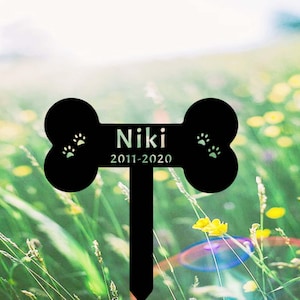 May include: Black metal bone-shaped garden marker with the name "Niki" and the dates "2011-2020" engraved on it.  The marker has paw prints on each side.
