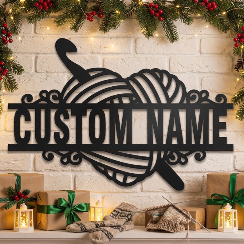 Pode incluir: Um letreiro de parede em metal preto com um novelo de l&atilde; estilizado e uma agulha de croch&ecirc;. O design inclui uma barra horizontal no centro com o texto CUSTOM NAME em fonte negrito sem serifa, acentuado por elementos decorativos em volutas.