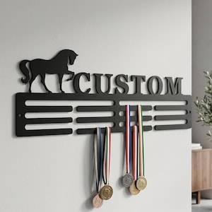 May include: A black metal wall-mounted medal display hanger featuring a silhouette of a horse on the left side and the word CUSTOM in capital letters. The rack includes multiple horizontal slots for hanging ribbons and medals with attached lanyards.