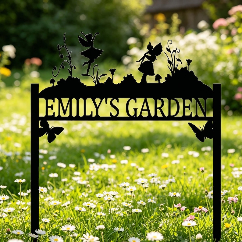 Puede incluir: Letrero de jard&iacute;n de metal negro con el texto "EMILY'S GARDEN". El letrero presenta siluetas de hadas, mariposas y plantas. El letrero est&aacute; colocado en un jard&iacute;n con hierba verde y flores blancas.