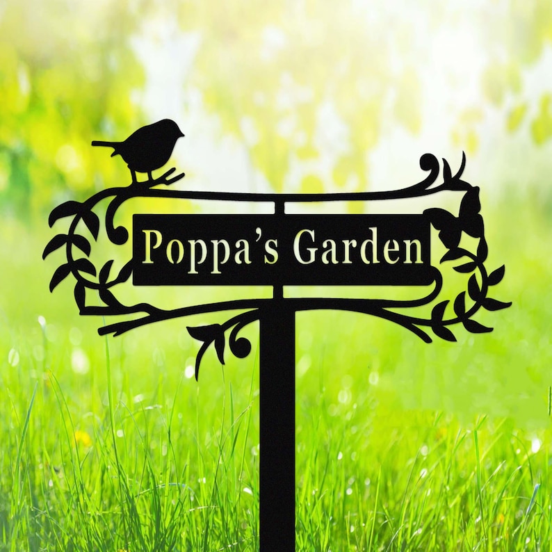 Puede incluir: Letrero de jard&iacute;n de metal negro con el texto "Poppa's Garden". El letrero presenta una silueta de un p&aacute;jaro posado en una rama, con hojas decorativas y una mariposa. El letrero est&aacute; montado en una estaca para una f&aacute;cil colocaci&oacute;n en un jard&iacute;n.