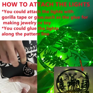 Op de afbeelding: Een close-up van een zwart houten hert-silhouet met groene lichtslingers eromheen gewikkeld. De afbeelding laat zien hoe je de lichten kunt bevestigen met tape of lijm. De tekst in de afbeelding luidt: "HOW TO ATTACH THE LIGHTS *You could attach the lights with gorilla tape or glue, such as the glue for making jewellery or toy *You could glue the lights along the pattern line"