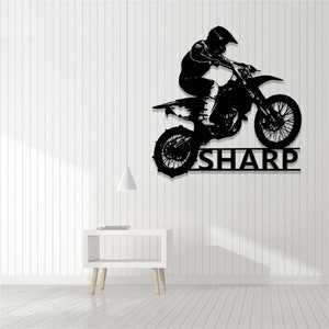 Op de afbeelding: Zwarte silhouet van een motorcrosser die springt op een crossmotor met de naam "SHARP" eronder.