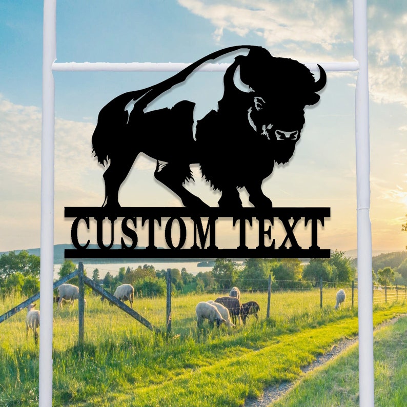 K&ouml;nnte beinhalten: Schwarze Metallsilhouette eines Bisons mit dem Text "CUSTOM TEXT" darunter. Die Silhouette ist auf einem wei&szlig;en Pfosten vor dem Hintergrund eines gr&uuml;nen Feldes und eines blauen Himmels montiert.