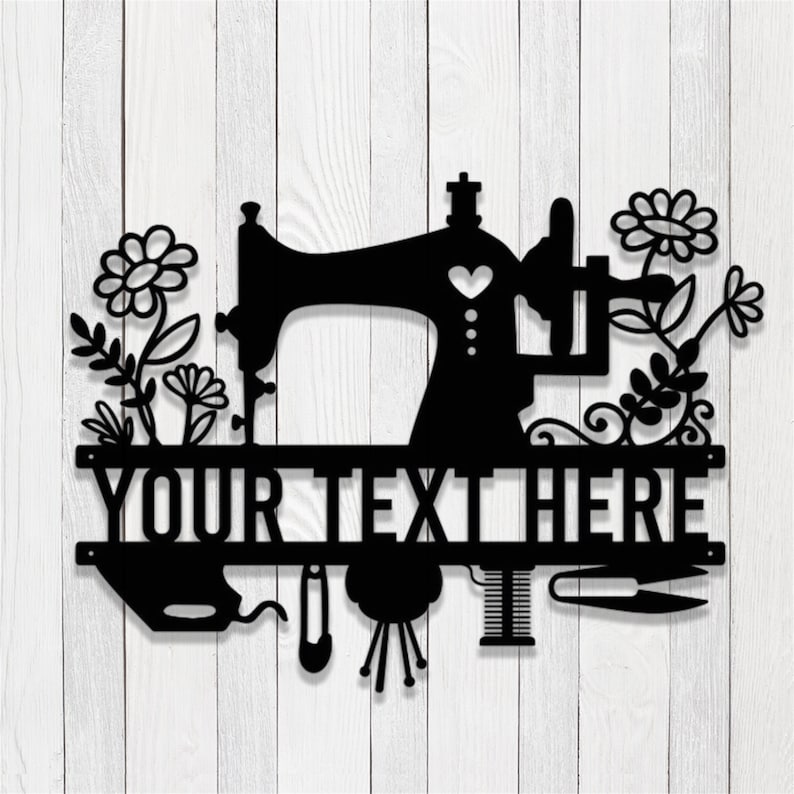 May include: Black metal sewing machine wall art with floral accents. Features the text "YOUR TEXT HERE" across the center. Includes a needle, thread, and scissors. Set against a white wood background.