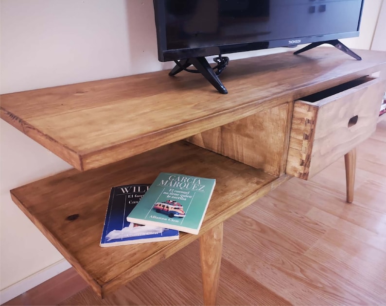 May include: A wooden TV stand with a drawer and a shelf. The stand has a light brown finish and is made of solid wood. The stand has a modern design and is perfect for any living room.