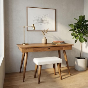 Op de afbeelding: Een houten bureau in mid-century modern stijl, met een bijpassende kruk. Het bureau heeft een warme houten afwerking, twee lades en schuine poten. Een goudkleurige bureaulamp, een ingelijste architectuurprint en een potplant zijn ook aanwezig.