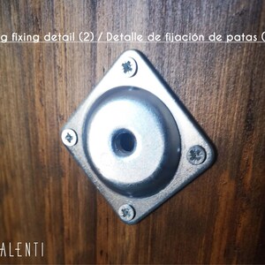 May include: Close-up of a silver metal leg fixing detail with a screw hole in the centre. The detail is attached to a dark brown wooden surface. The text "Leg fixing detail (2) / Detalle de fijaci&oacute;n de patas (2)" is visible above the detail.