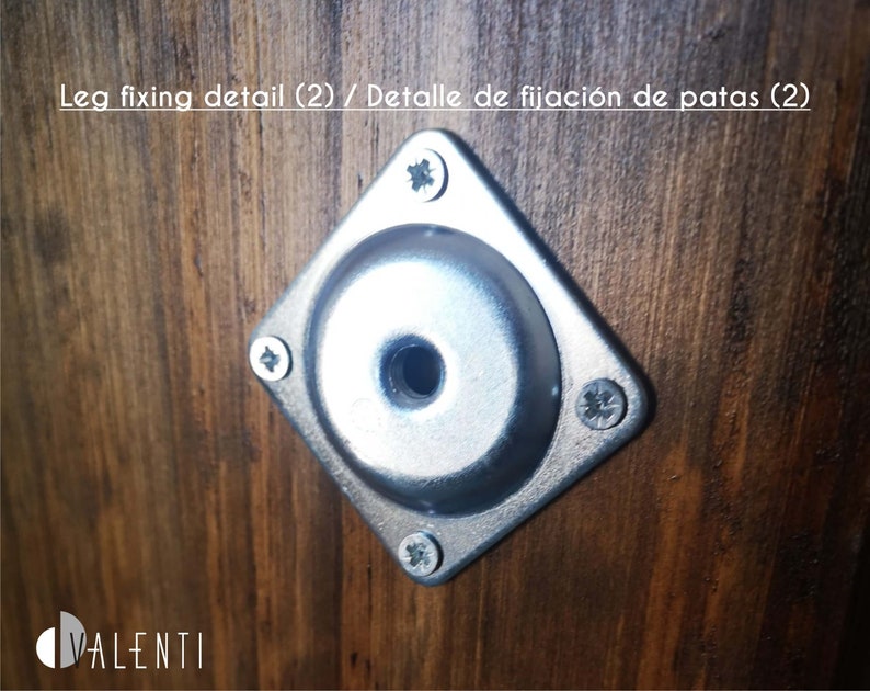 May include: Close-up of a silver metal leg fixing detail with a screw hole in the centre. The detail is attached to a dark brown wooden surface. The text "Leg fixing detail (2) / Detalle de fijaci&oacute;n de patas (2)" is visible above the detail.