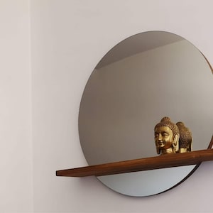 May include: A round mirror with a wooden shelf underneath. Two gold statues of Buddha are on the shelf.