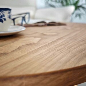 May include: Close-up of a round wooden table top with a natural wood grain pattern. The surface is smooth and appears to be made of solid wood.