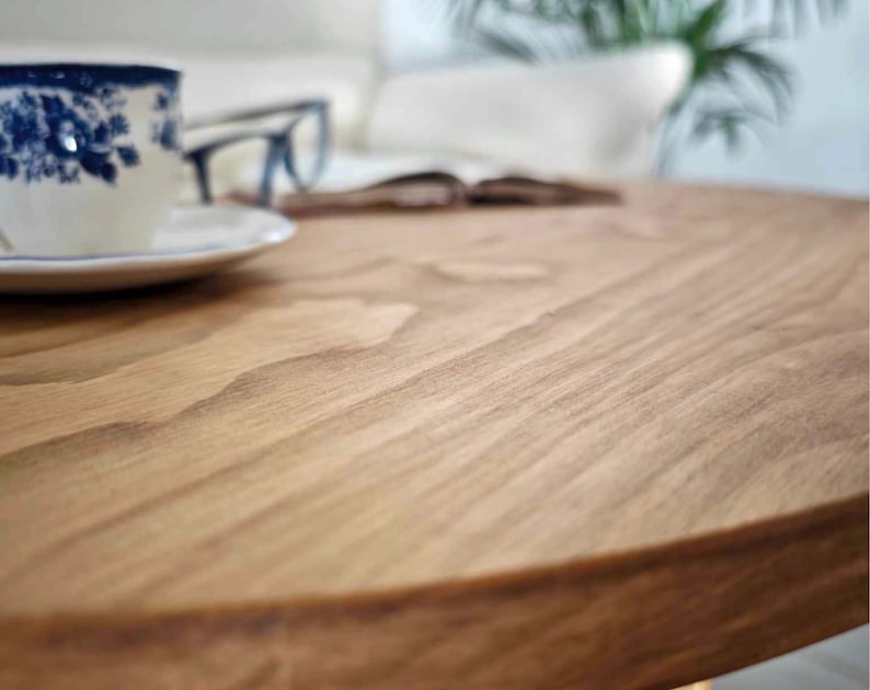 May include: Close-up of a round wooden table top with a natural wood grain pattern. The surface is smooth and appears to be made of solid wood.