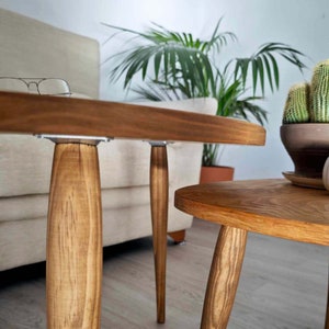 May include: Two wooden coffee tables with a natural wood finish. The larger table has a rounded rectangular top and the smaller table has a round top. Both tables have four legs.