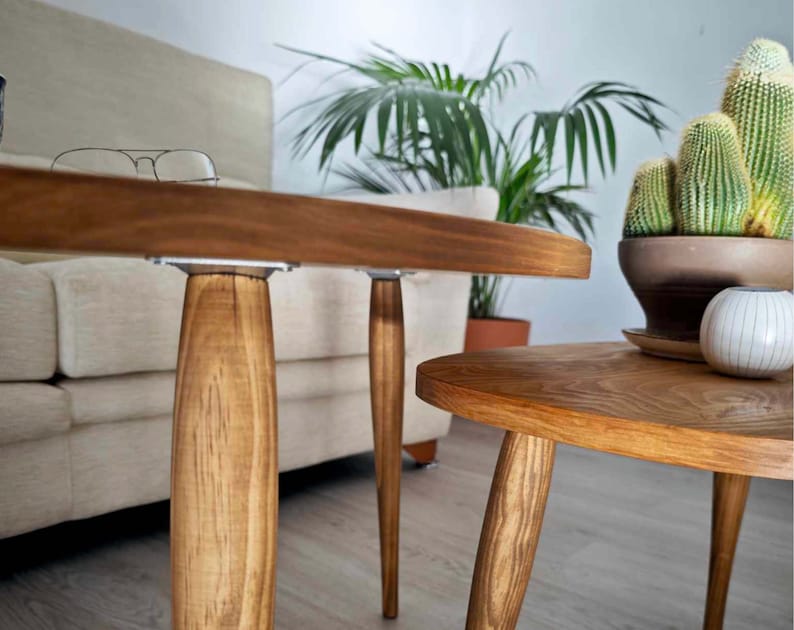 May include: Two wooden coffee tables with a natural wood finish. The larger table has a rounded rectangular top and the smaller table has a round top. Both tables have four legs.