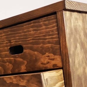 May include: A wooden dresser with three drawers. The top drawer has a small cutout handle. The dresser is stained a dark brown color.