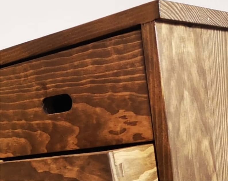 May include: A wooden dresser with three drawers. The top drawer has a small cutout handle. The dresser is stained a dark brown color.