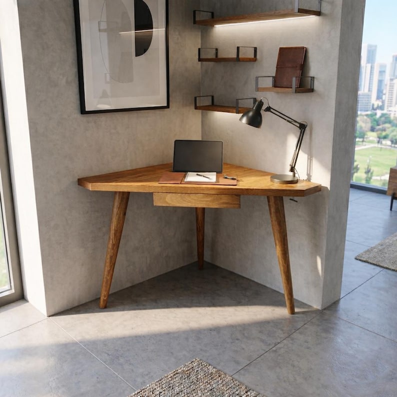 May include: A wooden corner desk with a triangular top and tapered legs. A laptop, notepad, and pen sit on the desk. A black desk lamp is positioned on the desk. The desk is in a modern office setting.