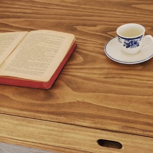 May include: A wooden table with a drawer and a book lying open on the surface. A cup and saucer with a blue and white floral pattern are on the table.