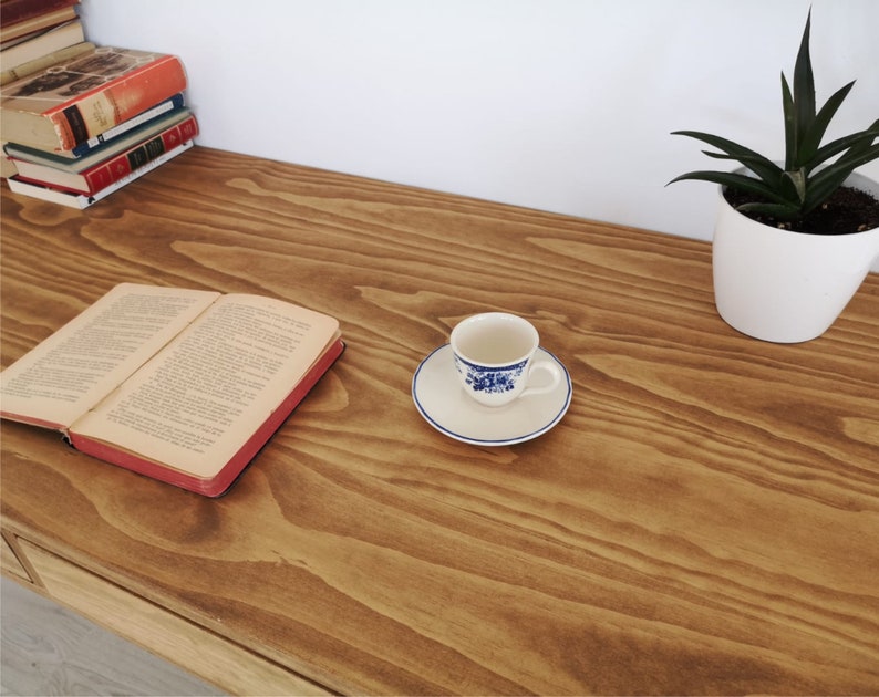 May include: A wooden desk with a book, a cup and saucer, and a potted plant. The desk has a natural wood finish and is made of solid wood.