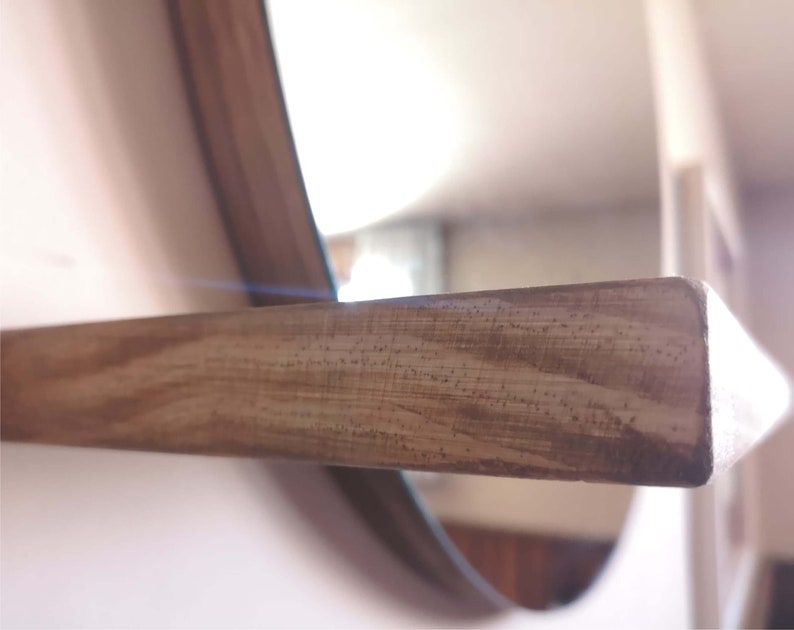 May include: A close-up of a wooden shelf attached to a round mirror. The shelf is made of light brown wood with a natural grain pattern.